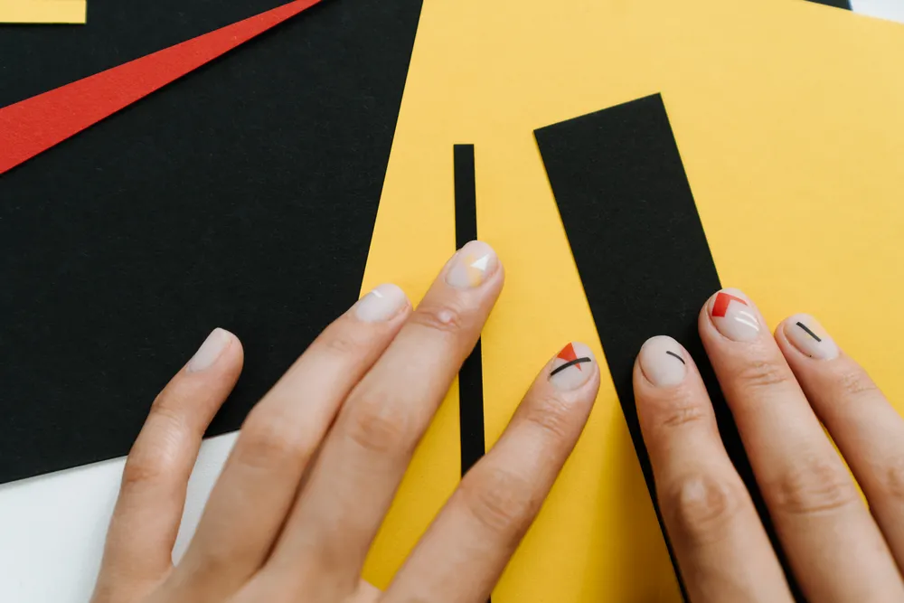 Short nails with minimal geometric red and black nail art on a bright background.