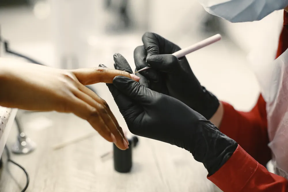 A nail technician in black gloves painting a client's nail at the salon.